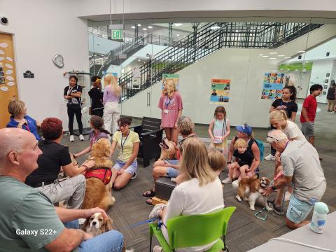 A group of individuals sitting in a circle with five dogs in the middle.