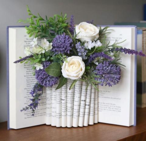 A book repurposed as a vase with purple flowers arranged between folded pages.