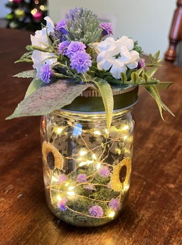 A mason jar with lights inside decorated with purple and white flowers 