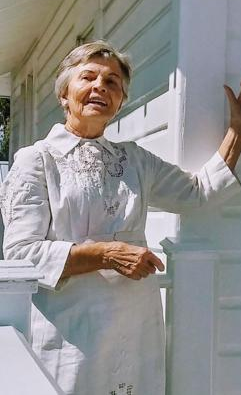 a women in a white historic dress stands outside a local history museum