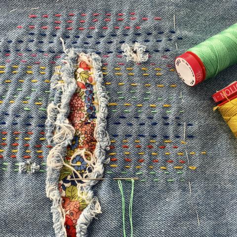 A hole in denim is mended shut with colorful threads.
