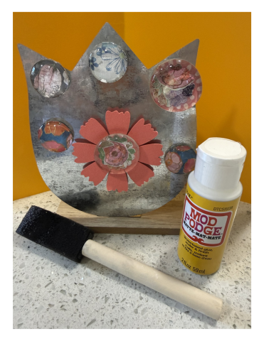 Glass magnets on a metal stand with a bottle of Modge Podge, and foam brush. 