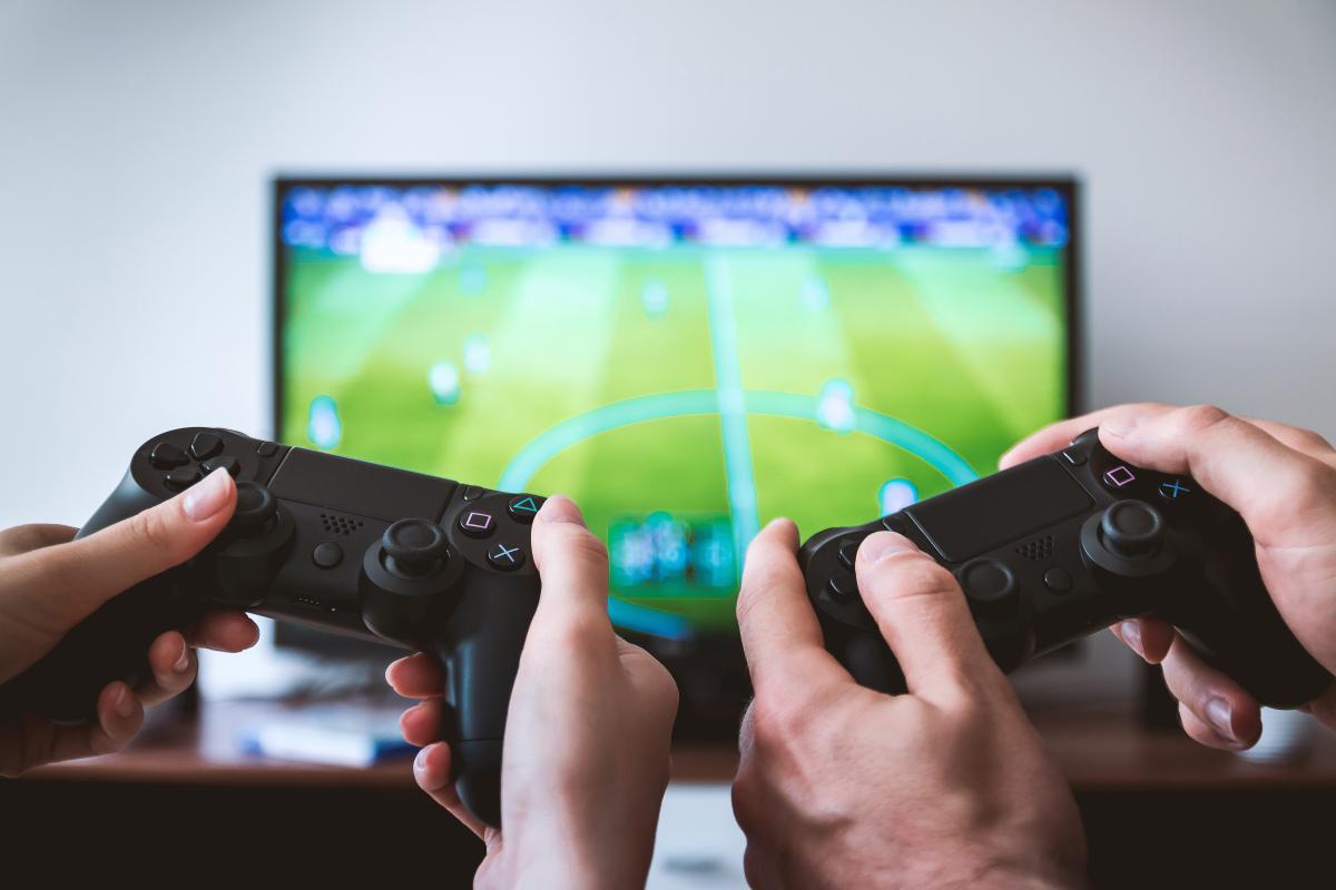 Two hands holding game controllers with the video game in the background.