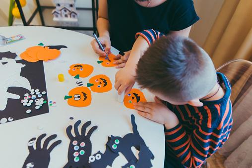 A child putting googly eyes on a paper cut out of a pumpkin.