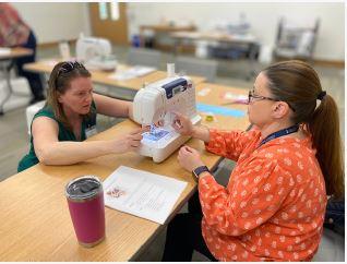 Two women learning how to use a sewing machine.