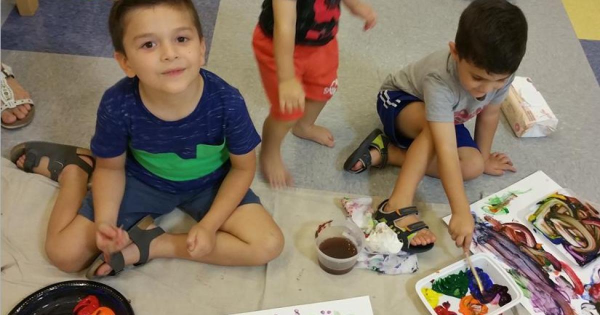 Two young boys sitting on the floor painting with fingerpaints.