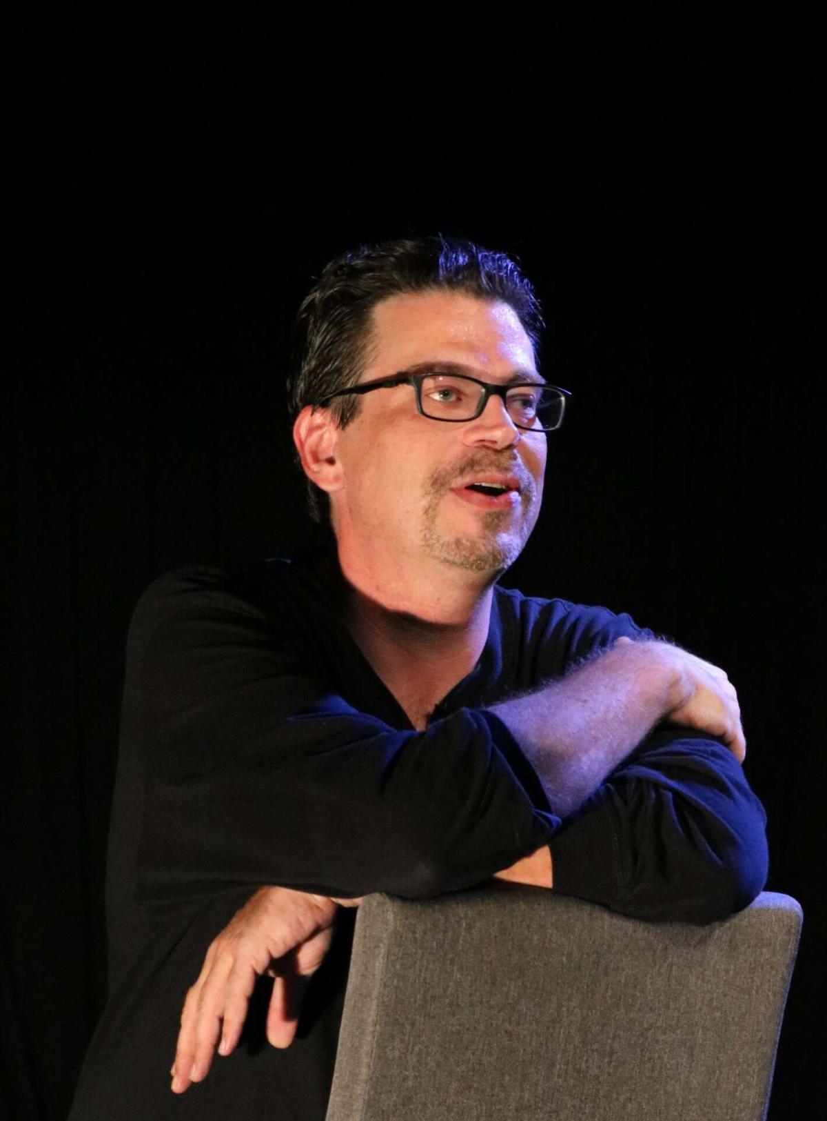 Playwright Glenn Schudel sits on a backward facing chair.