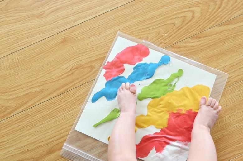 Paper with paint inside a resealable baggie with a pair of baby feet standing on it.