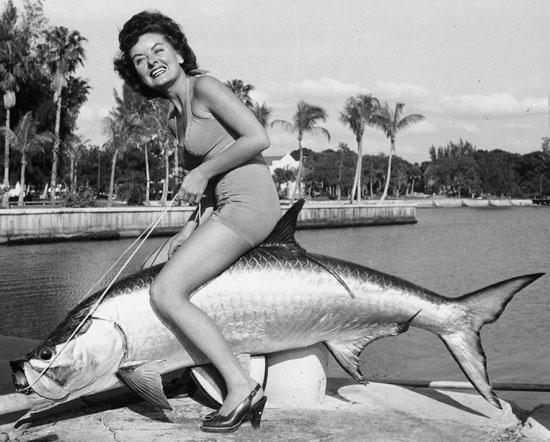 A black and white image of a woman posing with a fake tarpon.