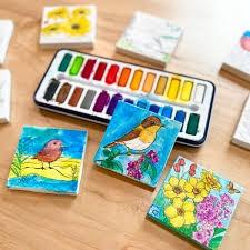 Three hand-painted canvas prints next to a set of watercolor paints.