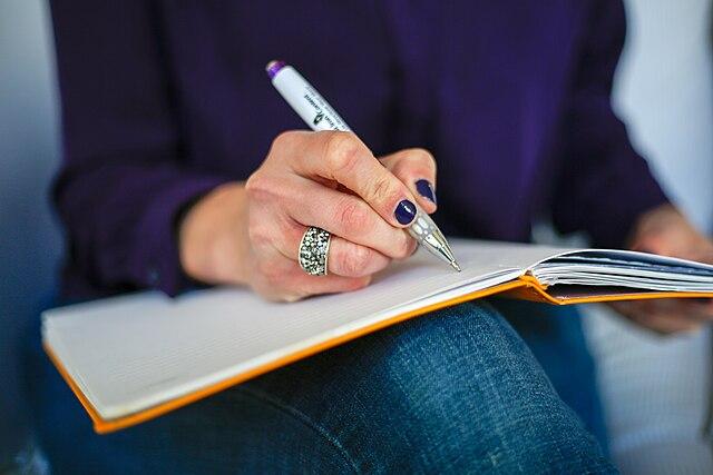 Woman writing in a notebook with a pen.