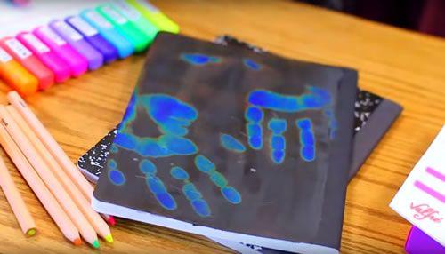 Pencils next to black notebook with blue handprint on it 