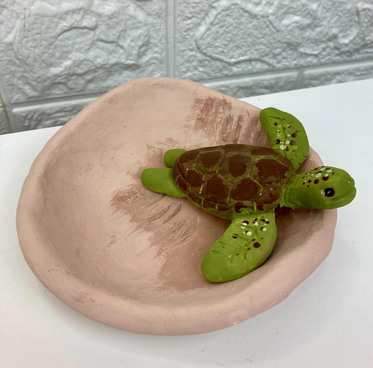a green clay turtle in a brown clay bowl