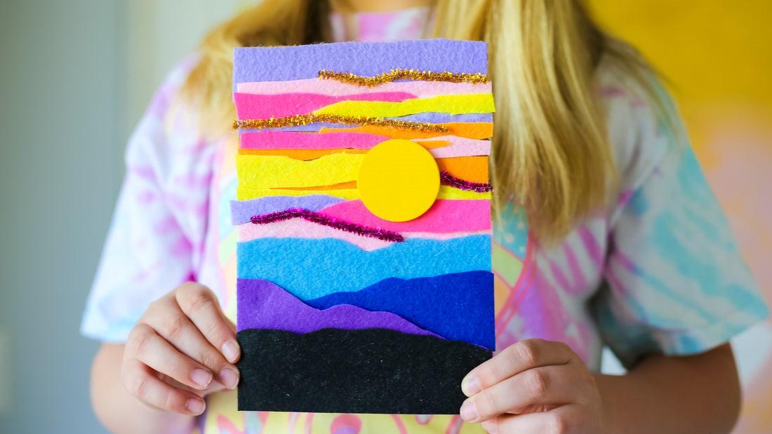 Person holding a felt collage picture of a sunset in various colors.
