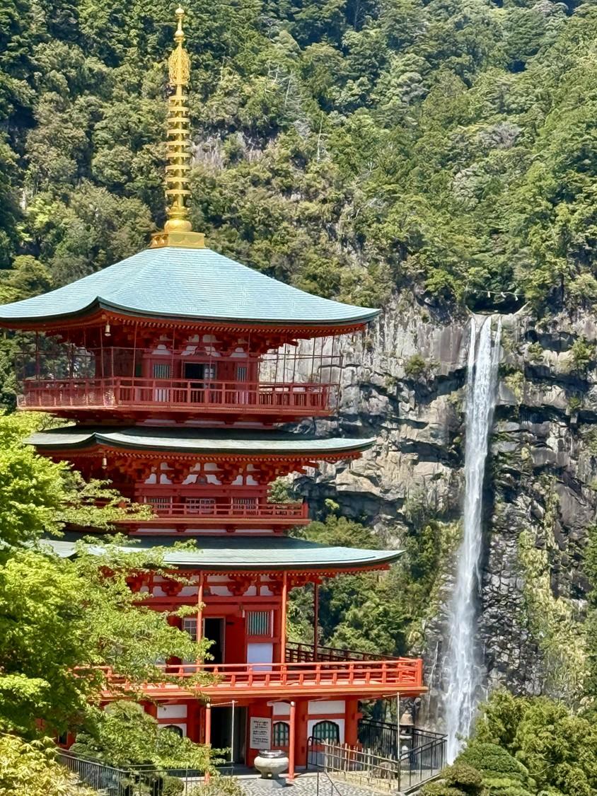 A red pagoda next to a cliffside with a waterfall.
