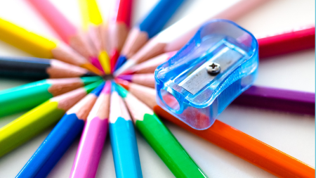 A variety of colored pencils on a white table with a pencil sharpener.