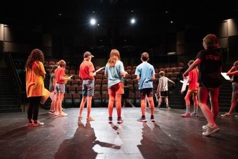 A group of tweens stands on a stage holding scripts.